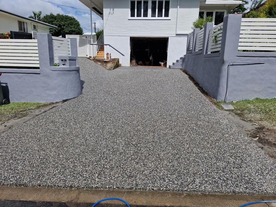 Exposed aggregate driveway running between grey rendered walls to a garage