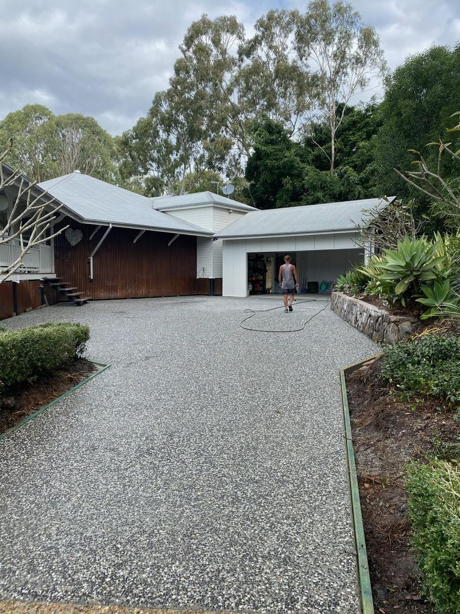 Wide exposed aggregate driveway leading to a double garage under tall trees